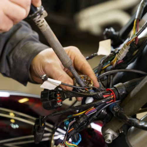 An electrician is soldering electrical wires to electrical equipment in a motorcycle. Close-up. Transport concept